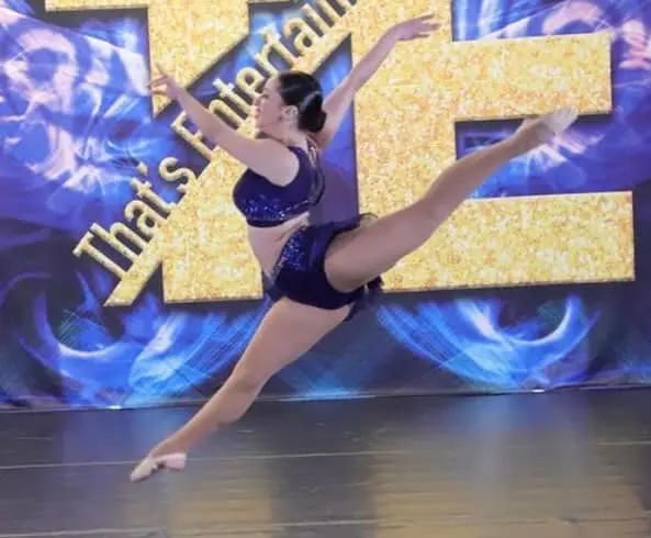 A woman in blue leotard and shorts jumping on stage.